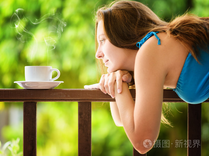 年轻女子在庭院里喝咖啡。户外人像
