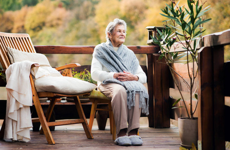 在秋日的一个阳光明媚的日子里, 一位老年妇女坐在户外的露台上