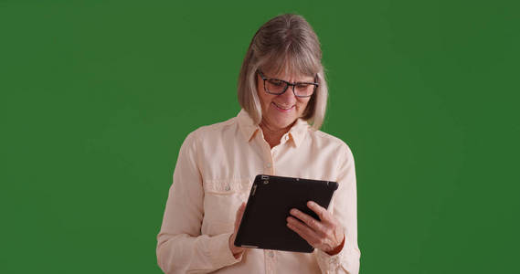 漂亮的老白人女士浏览网页上的平板电脑上的绿色屏幕