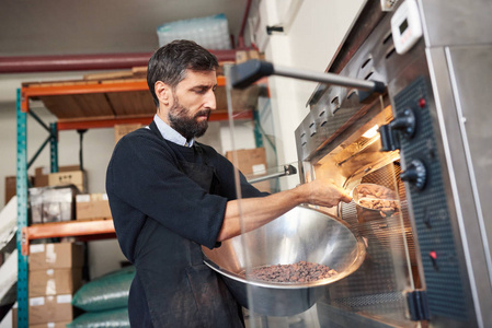 一家手工制作巧克力的工厂的小企业主将可可豆从碗里放入烘焙机中