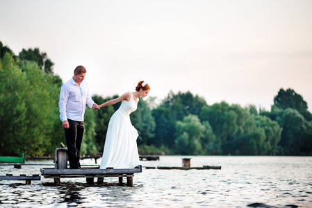 美丽的年轻夫妇，新娘和新郎湖背景上摆姿势。新郎和新娘在码头上