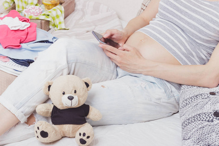 怀孕妇女与泰迪熊和各种各样的衣裳为新生儿, 顶部看法