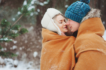 快乐的年轻情侣漫步在白雪皑皑的冬季森林, 覆盖着特大的围巾和拥抱。户外活动冬季假期