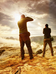 摄影师在悬崖上, 相机取景器在他的脸上。自然摄影师在岩石的峰值拍摄与镜子相机的照片。梦幻般的顽固景观