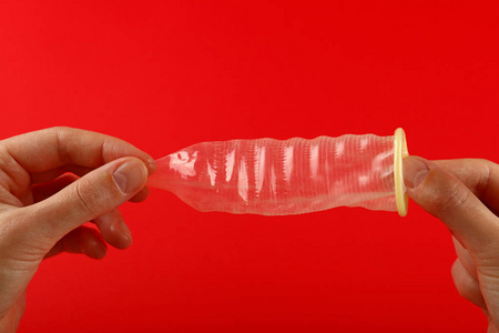 关闭两个女人手拿着一个开放的乳胶避孕套在红色背景与复制空间, 低角度侧面视图