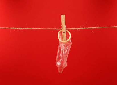 关闭一个避孕套挂在缠绕洗涤线与木 clothespin 的红色背景与复制空间, 低角度侧面视图