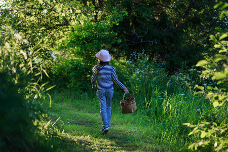 年轻女孩走在一条小路上, 穿过绿色的树林背着篮子