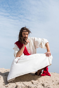 耶稣在长袍, 红色窗扇和刺冠举行念珠和显示沈默标志在沙漠