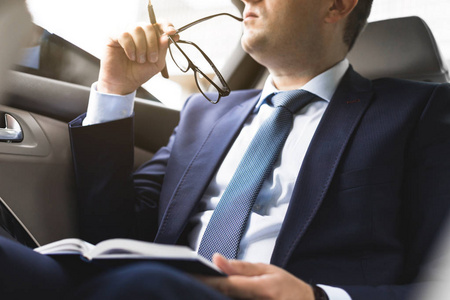 穿着西装的男人在笔记本电脑上写着笔记本电脑, 在一辆昂贵的汽车的沙龙里, 有皮革内饰