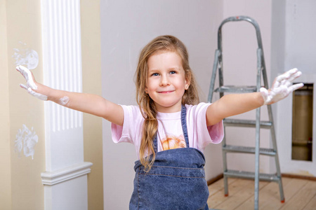 在公寓里修理。幸福的家庭母亲和女儿在围裙油漆墙壁与白色油漆。女孩在油漆中显示她的手掌, 笑了。肖像