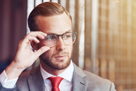 自信和时尚。一个专业英俊的商人站在办公室里拿着眼镜看的肖像