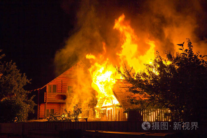 晚上烧木房子明亮的橙色火焰和浓密的烟雾下的瓷砖屋顶在黑暗的天空