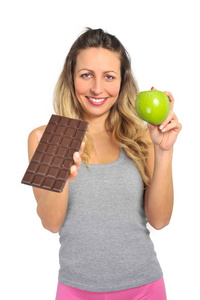 有魅力的女人抱着苹果和巧克力棒在健康的水果与甜味垃圾食品的诱惑