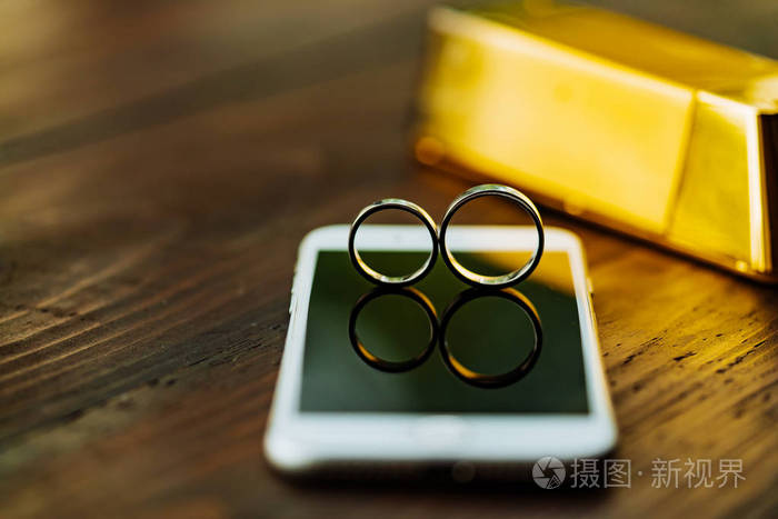 两个结婚戒指在电话上显示。一双金戒指在房间的木桌的背景上。