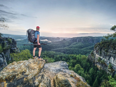 沉重的背包和三脚架在手中的高大摄影师站在岩石角度和观看到深雾谷
