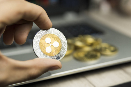 男性商人手持波纹硬币的背景下笔记本电脑键盘和成堆的金币。虚拟货币和金融增长概念。贸易开采波纹