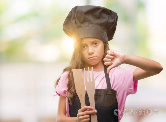 褐发女郎西班牙女孩穿着厨师制服与愤怒的脸, 消极的迹象显示不喜欢大拇指下来, 拒绝的概念