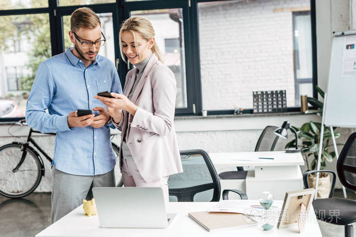 微笑的年轻商业同事使用智能手机和谈话在办公室照片-正版商用图片0