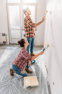 新公寓中年轻夫妇拿着油漆辊墙面的高角度视角