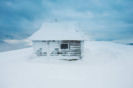 山上的一座小房子。一个冰雪覆盖的小屋, 背景是一个冬天的森林和一个美丽的天空与云。山风景