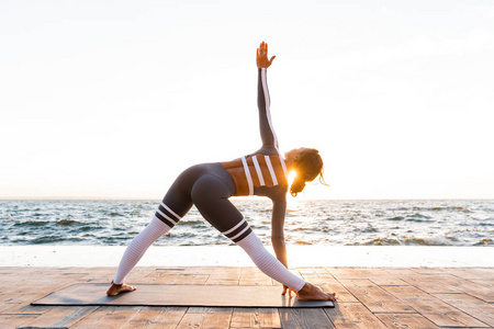 在海滩上的惊人强壮的年轻健身妇女的形象做瑜伽伸展运动