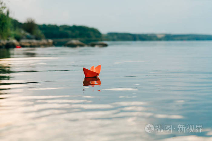 夏天, 一艘纸船在河边航行.它有一个橙色的颜色和漂浮沿岸边下游