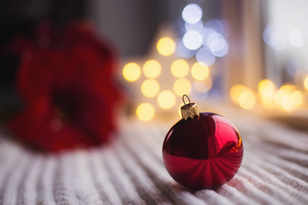 红色圣诞球白色针织面料在日光与温暖的花环散景背景。节日魔术灯。新年假期贺卡