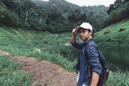 年轻的亚洲冒险家的肖像看着相机与自然绿色山背景。旅行生活方式和放松的概念
