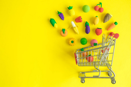 创意布局购物车与橡胶蔬菜和果在黄色背景最低创意概念。复制空间