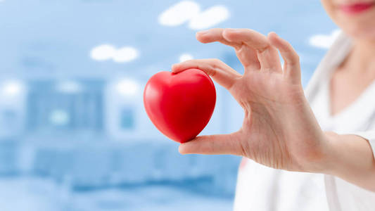 医生在医院办公室拿着一颗红色的心脏。医疗保健和医生工作人员服务概念