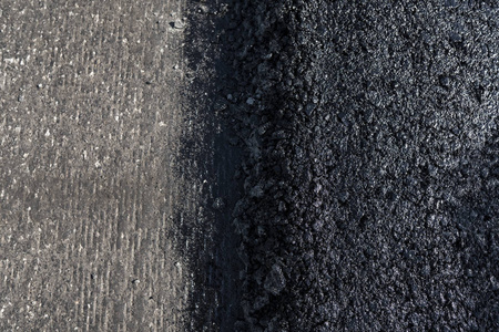 新铺设的黑色沥青沥青与高边缘的砾石显示的结构。在公路上铺设新的沥青。公路建设