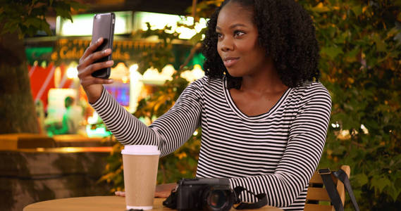 可爱的黑人女子晚上在食品摊附近拿着智能手机自拍自拍