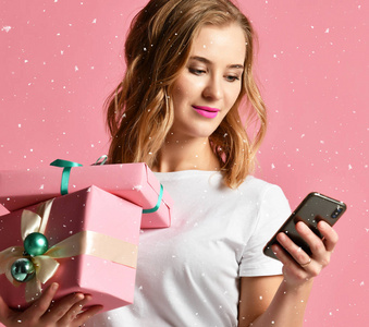 妇女网上购物与手机圣诞节礼物礼物微笑在浅粉红色