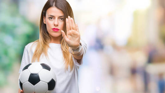 年轻的美女拿着足球越过孤立的背景, 张开手做停止标志, 用严肃而自信的表情, 防守姿态