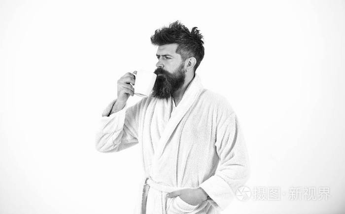 穿着浴衣的帅哥拿着一杯白色背景的杯子。有胡子的家伙早上喝咖啡或喝茶。清晨宁静