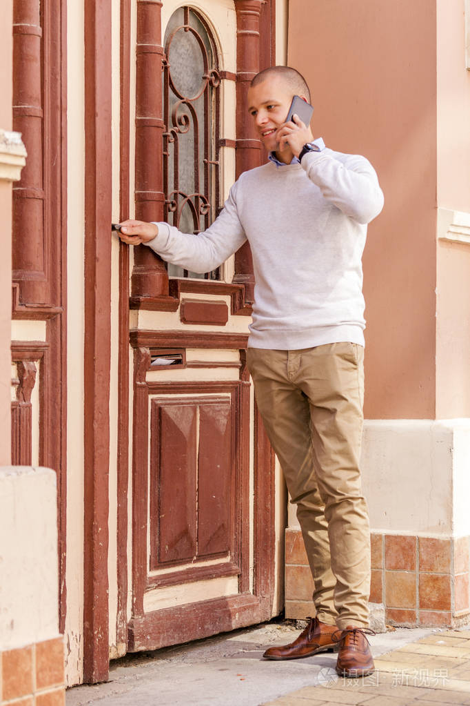 帅气的年轻商人打开门, 用手机交谈.他是来上班的