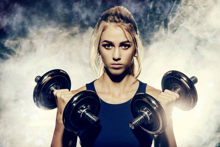 女性身形与美丽矫健的身形与哑铃锻炼肌肉的年轻女子.健身, 健美.