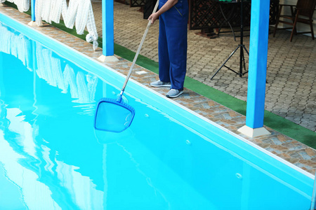 男工人清洁户外泳池与铲网