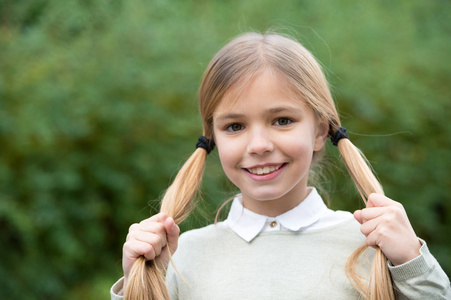 女孩愉快的微笑与金发马尾在绿色自然背景.可爱的女生发型.