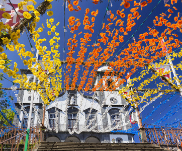 装饰黄色, 橙色, 蓝色和白色的花朵串起导致我们的蒙特卡洛圣母教堂在葡萄牙的丰沙尔