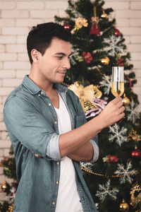 满意的白种人与美丽的装饰圣诞树的背景, 愉快地看着一杯白葡萄酒, 享受他在圣诞节的特殊时光。圣诞节主题
