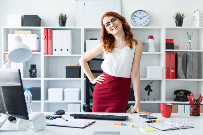 漂亮的小女孩站在桌子旁边的办公室里女孩把一只手放在她的臀部第二个