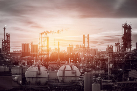 石油化工或石油天然气精炼厂储气球罐在傍晚时分, 在日落天空背景下制造天然气柱和烟雾堆的石油工业工厂