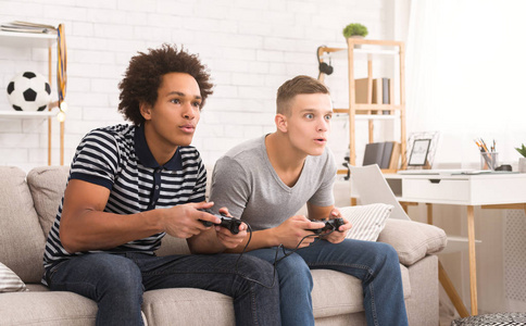 不同的十几岁的男孩在家里玩游戏机照片