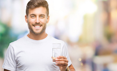年轻英俊的人喝玻璃水在孤立的背景与一个快乐的脸站立和微笑着自信的微笑显示牙齿
