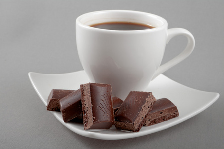 一碟在灰色的背景上的黑色咖啡与巧克力位于