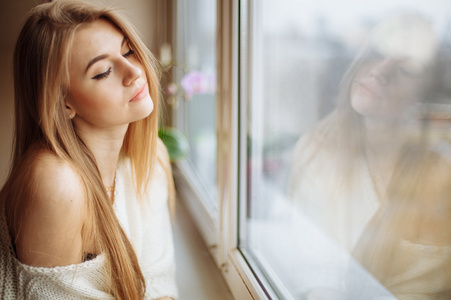 美丽的金发女人在早上坐在窗边喝着茶