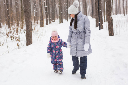 家庭, 冬天和自然概念年轻开朗的母亲与可爱的小女儿走在雪地公园