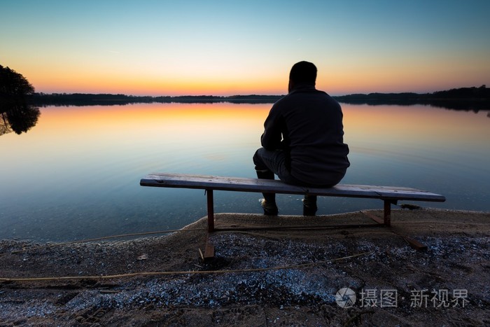 在日落时分在湖岸上的长椅上坐着的人