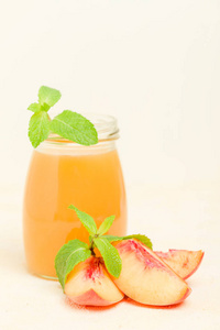 桃冰沙在玻璃罐子与新鲜成熟的果子和绿色薄荷叶子在黄色柔和的背景原始的甜甜点或早餐饮料为健康有机饮食概念
